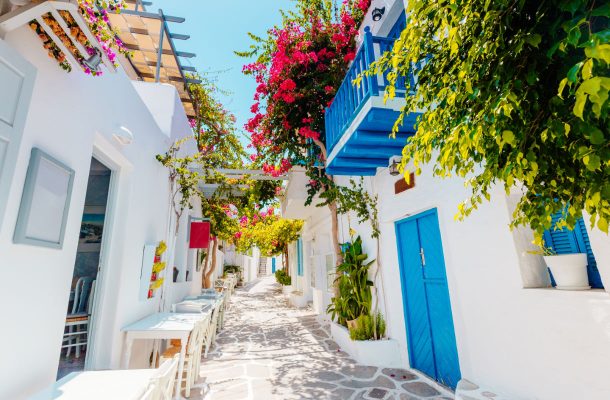 Kreikkalainen kapea katu, valkoiset seinät, siniset ovet ja paljon kukkia