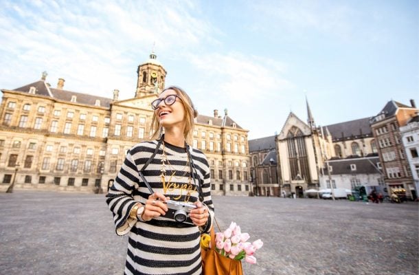 Hymyilevä nainen kamera kädessä katselemassa maisemia Amsterdamin Dam-aukiolla.