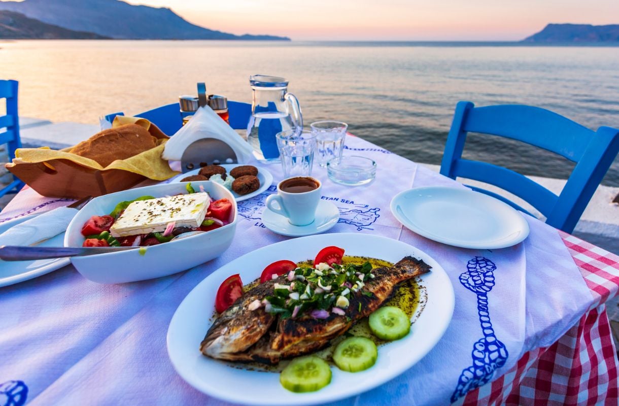 Kreetalainen ruokapöytä täynnä ruokaa auringonlaskussa. Kala-ateria kurkuilla ja fetasalaatti.