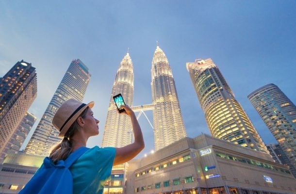 Nainen ottamassa kuvaa kännykällä iltahämärässä valaistuneista kahdesta jättitornista.