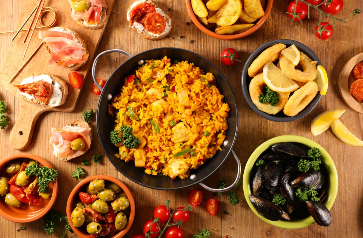 Espanjalaista ruokaa aseteltuna vierekkäin pöydälle, kuva otettu ylhäältä päin. Värikäs valikoima eri ruokia. 