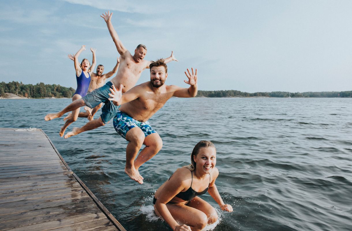 Hymyilevät kaverukset hyppäämässä laiturilta veteen.